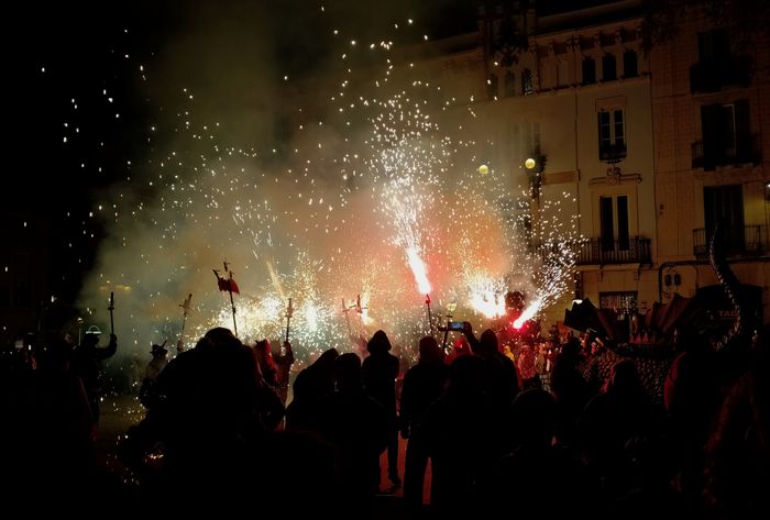 "Photo of the central plaza of Gràcia neighbourhood during the final act of the correfoc. There are dragons, and fire, and lightning sparkles shooting up the height of the 4 story buildings of the plaza